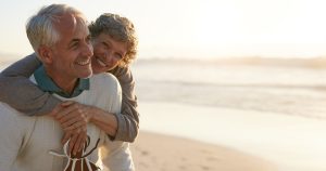 Portrait of happy mature man being embraced by his wife at the beach. Senior couple having fun at the sea shore.